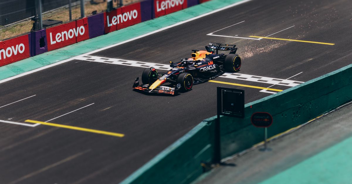 Formula 1 car speeding across the finish line on a racetrack, emitting sparks.